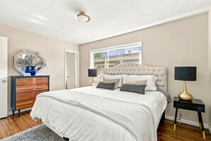 A bedroom with a large bed, a dresser, a mirror, and a window with blinds. - Spacious Furnished 5BR Denver Home, Pet-Friendly, Fenced Yard & Garage (Denver)