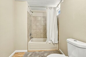 Een badkamer met een bad, toilet en douchegordijn.