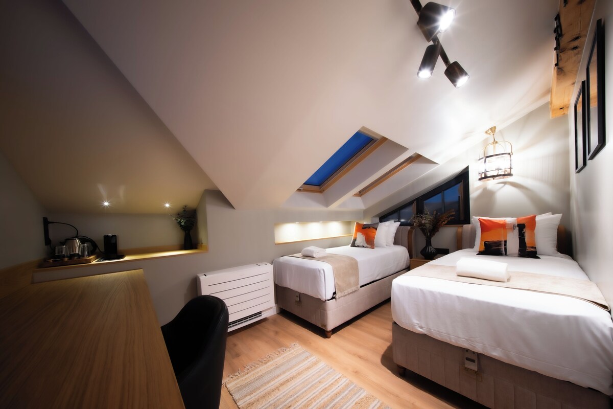 Quarto moderno com duas camas, uma escrivaninha e um claraboia.