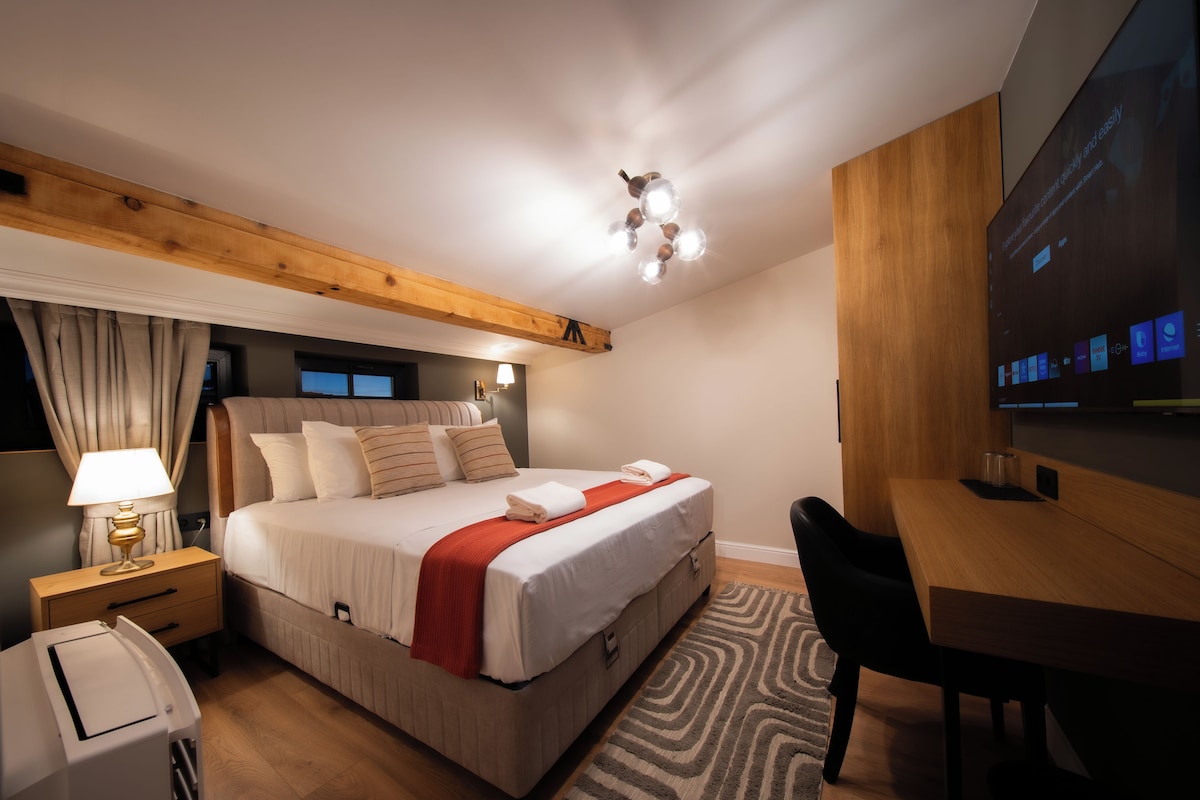 Quarto de hotel moderno com uma cama grande, uma escrivaninha, uma televisão e teto de madeira.