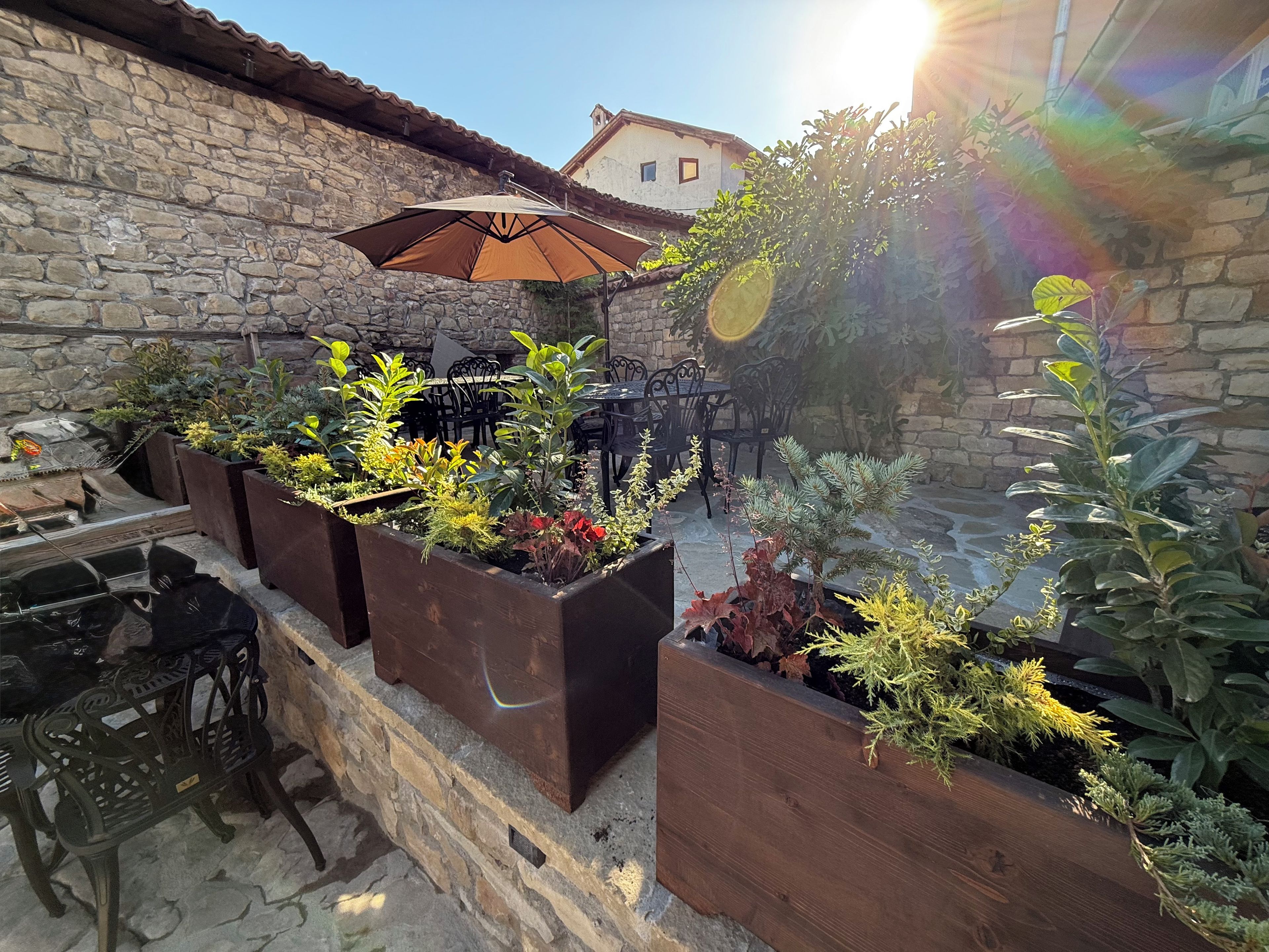 Eine Terrasse im Freien mit Steinmauern, Holz-Pflanzkästen mit unterschiedlichen Pflanzen und Gartenmöbeln.