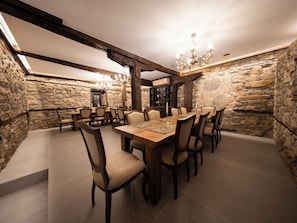 Uma sala de jantar com uma mesa de madeira comprida, várias cadeiras, um candelabro e paredes de pedra.
