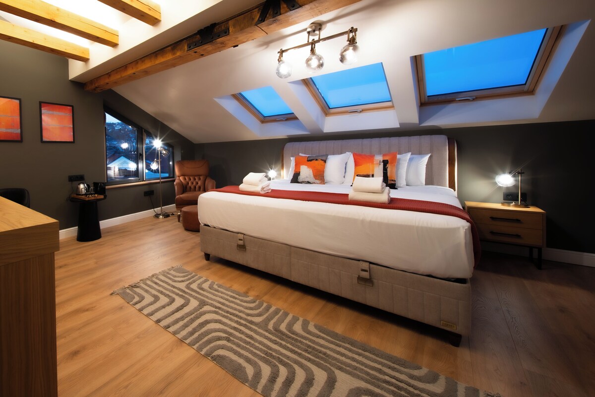 Quarto com cama grande, claraboias, escrivaninha e cadeira.