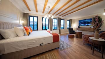 Ein modernes Hotelzimmer mit einem großen Bett, einer Sitzecke inklusive Sofa und Sessel, einem Fernseher und Blick ins Freie.