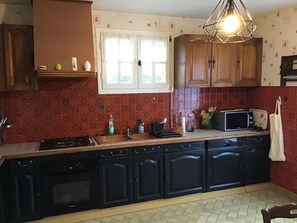 A kitchen with a gas stove, dishwasher, black cabinets, a microwave, and a hanging light fixture. - New Listing (Égletons)