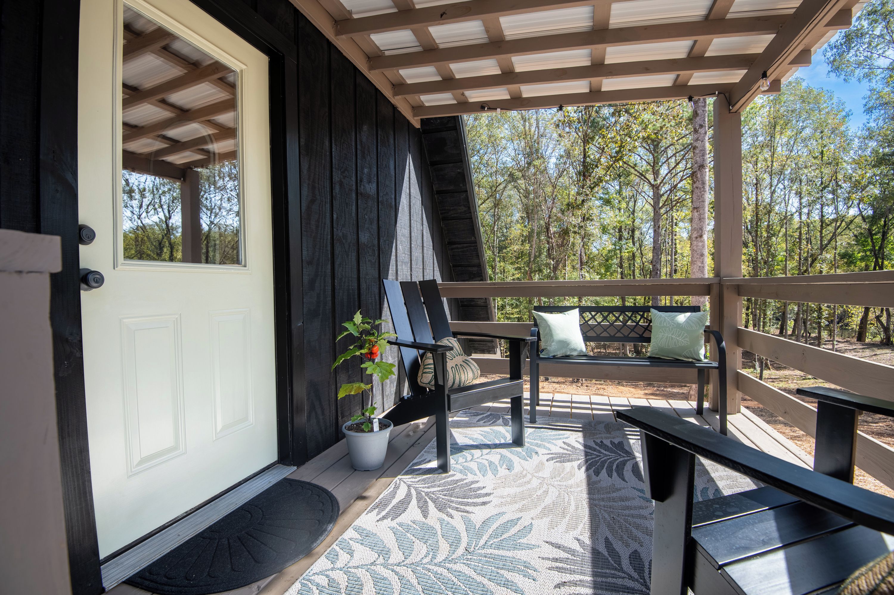 A covered porch with a bench, a potted plant, and a door leading to a building.