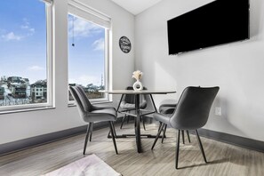 A modern room with a large window, a round table with chairs, and a mounted TV. - NV Hotel w/ Pool, Gym, Rooftop Lounge & Free Park (Nashville)
