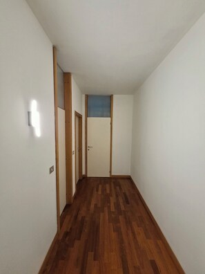 Un couloir avec un plancher en bois, des murs blancs et une porte avec un vitrail bleu au fond.