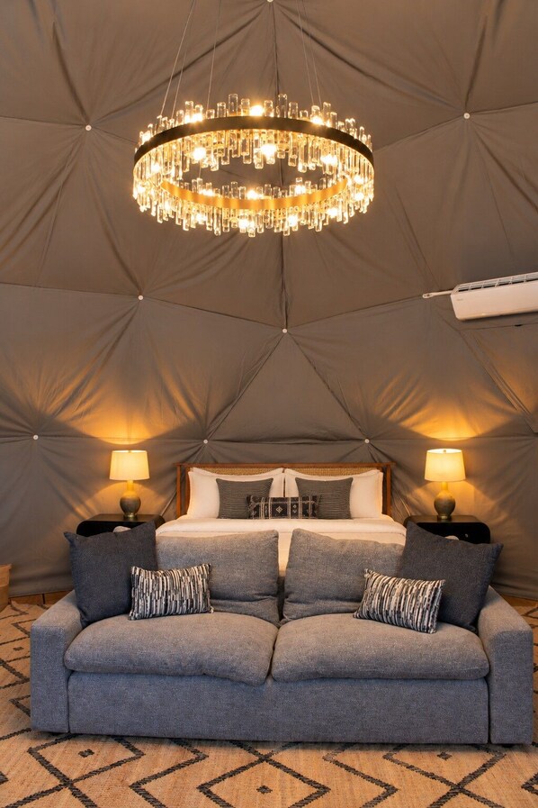 A tented room with a bed, two bedside lamps, a grey sofa with patterned cushions, and a chandelier. - Pine Hollow - Kelly Canyon Dome (Ririe)