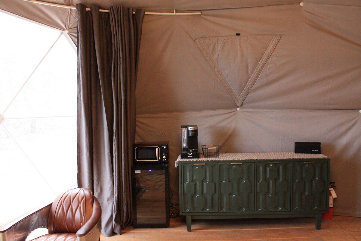 Una habitación con tienda, una kitchenette, un microondas, una cafetera, un armario verde y un sillón de cuero.