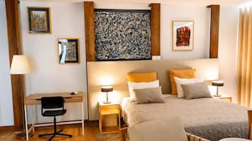 A hotel room with a bed, bedside tables, a desk, a chair, and artwork on the walls.