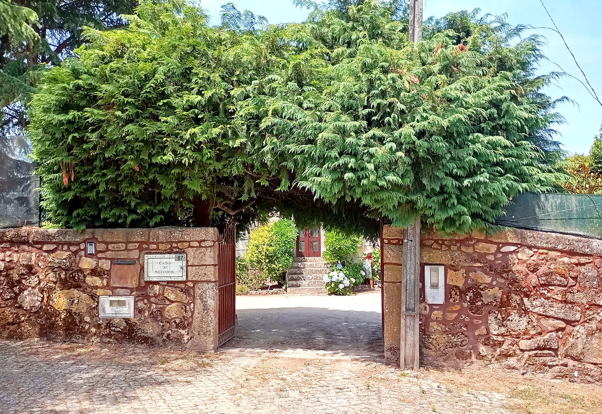 A stone archway leading to a building with a red door, surrounded by lush greenery.