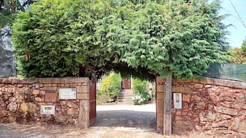 A stone archway leading to a building with a red door, surrounded by lush greenery.