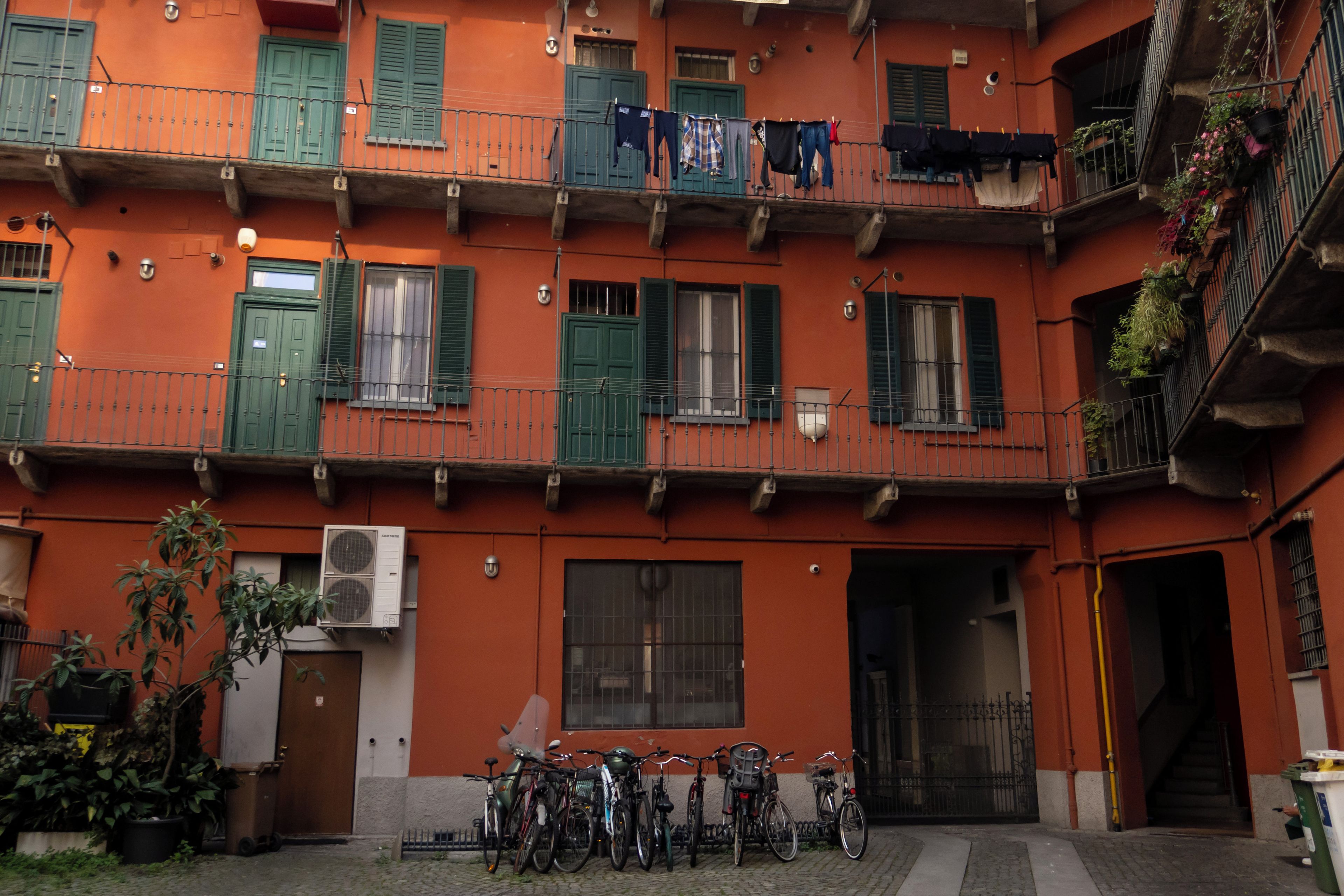 Un edificio de varios pisos con balcones, una fila de bicicletas estacionadas adelante y una puerta que da a un espacio interior.
