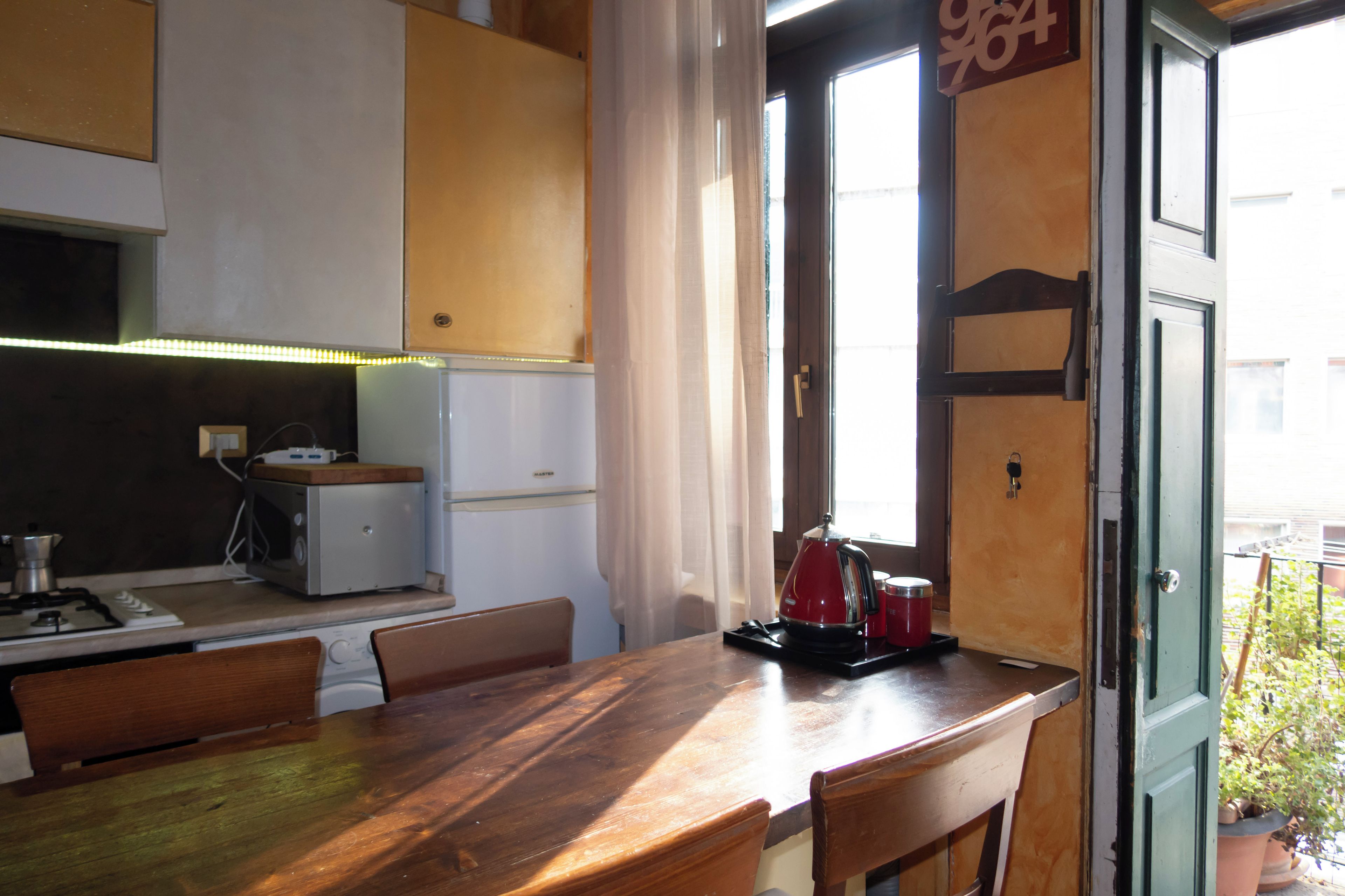 Una cocina compacta con una mesa de comedor, sillas, un refrigerador pequeño y una tetera.