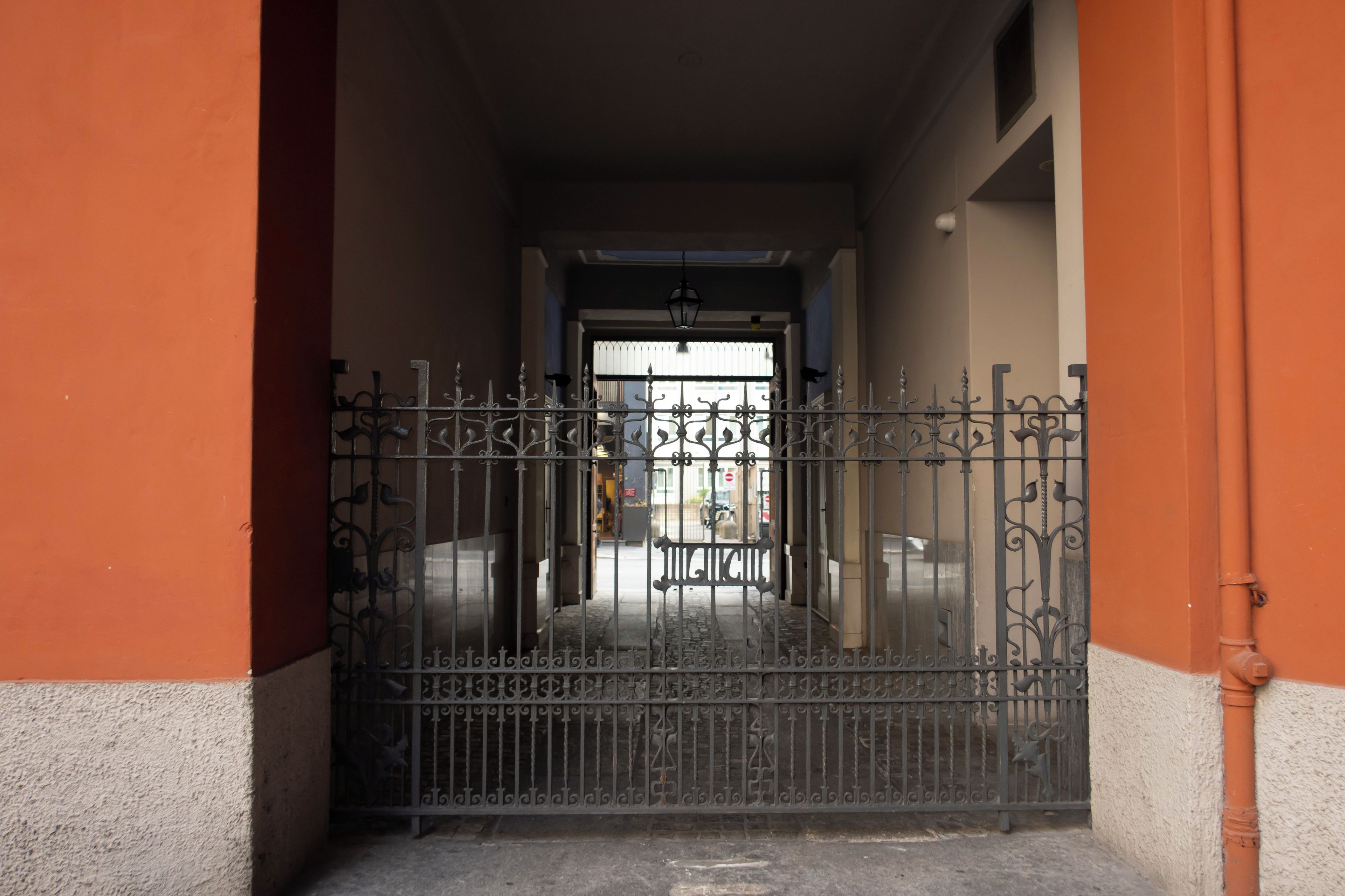 Une entrée fermée par un portail en métal et une porte, donnant accès à un immeuble.