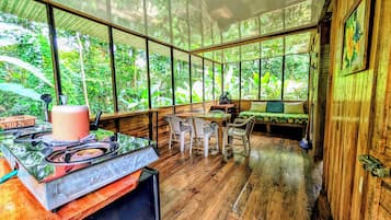 Una habitación con piso de madera, una mesa de comedor con sillas, un sofá y un ventanal con vista a la vegetación.