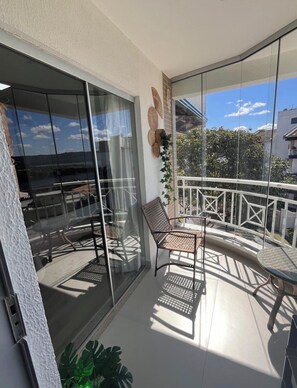 Un balcon avec une porte-fenêtre, une chaise, une table et un pot de fleurs.