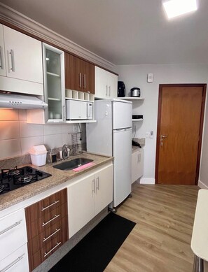 Une cuisine de taille réduite avec des meubles blancs, un four à micro-ondes, un réfrigérateur et une cuisinière.