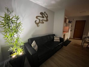 Un salon avec un canapé noir, un élément décoratif mural et un plant de bambou en pot.