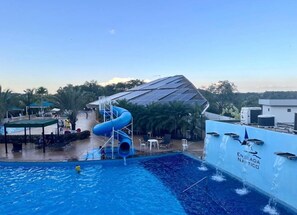 Piscina com escorrega azul, área de estar coberta e edifício com painéis solares.