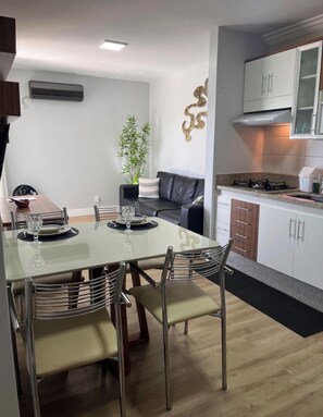 A modern kitchen with white cabinets, a gas stove, and a dining area with a glass table and metal chairs. - New Listing (Caldas Novas)