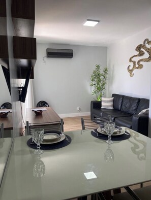 Un espace repas moderne avec une table en verre pour deux personnes, un canapé en cuir noir et un élément décoratif mural.