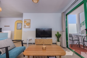 A modern living room with a flat-screen TV, a wooden coffee table, a sofa, and a dining area with a table and chairs. - 149 San Fermin, A/C, 500Mbps, Parking, 9 Mins to Beach, Ground Floor (Puerto del Carmen)