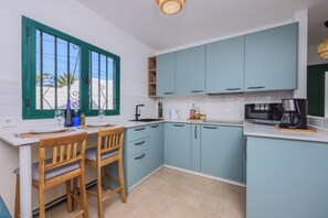 A modern kitchen with teal cabinets, a white countertop, and a dining area with wooden chairs. - 149 San Fermin, A/C, 500Mbps, Parking, 9 Mins to Beach, Ground Floor (Puerto del Carmen)