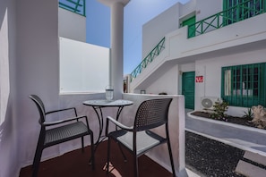 A terrace with two chairs and a table, a white building with green accents, and a green door. - 149 San Fermin, A/C, 500Mbps, Parking, 9 Mins to Beach, Ground Floor (Puerto del Carmen)