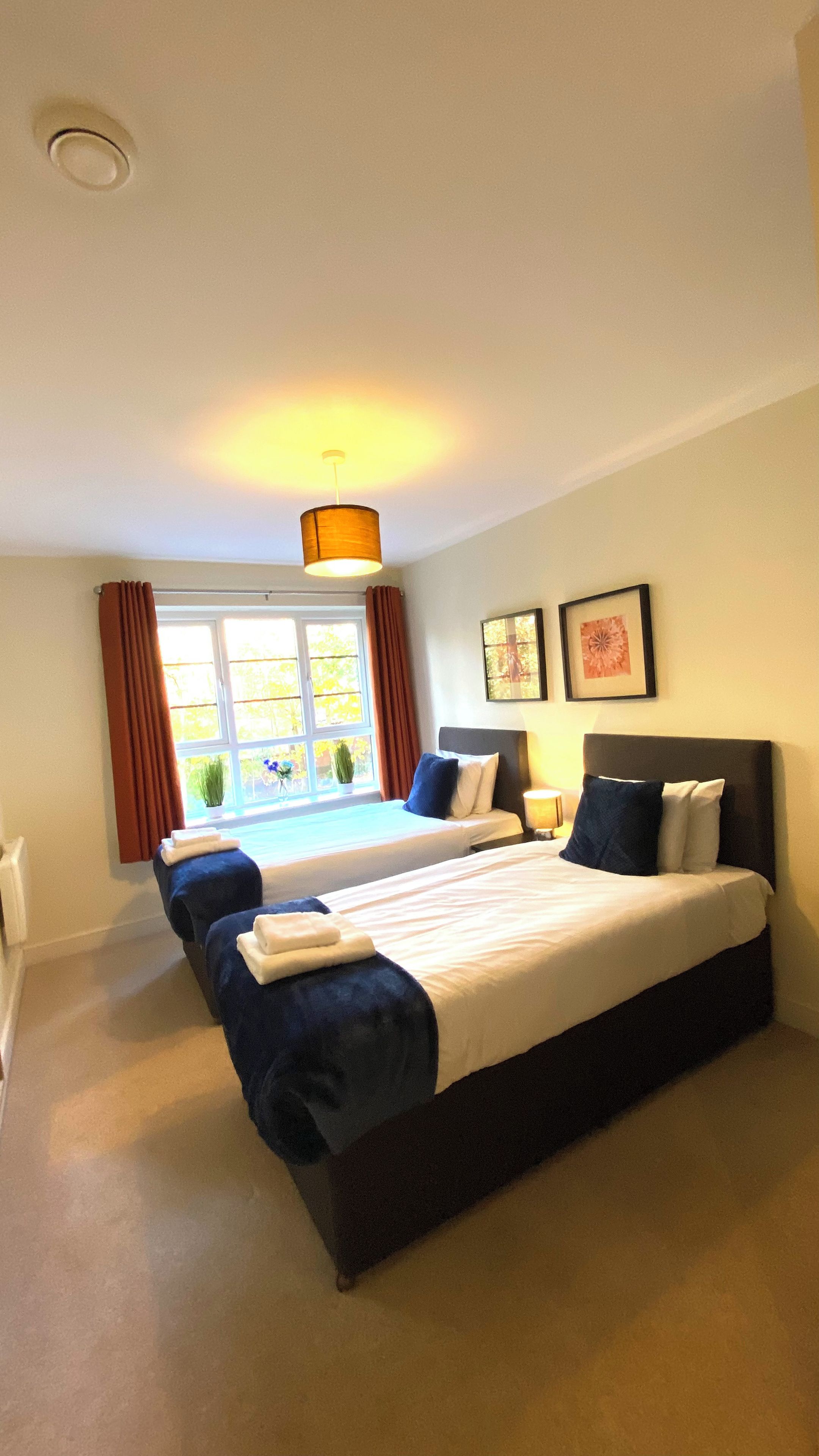 A hotel room with a large bed, a bedside table, a window with curtains, and a ceiling light.