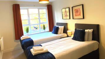 A hotel room with a large bed, a bedside table, a window with curtains, and a ceiling light.