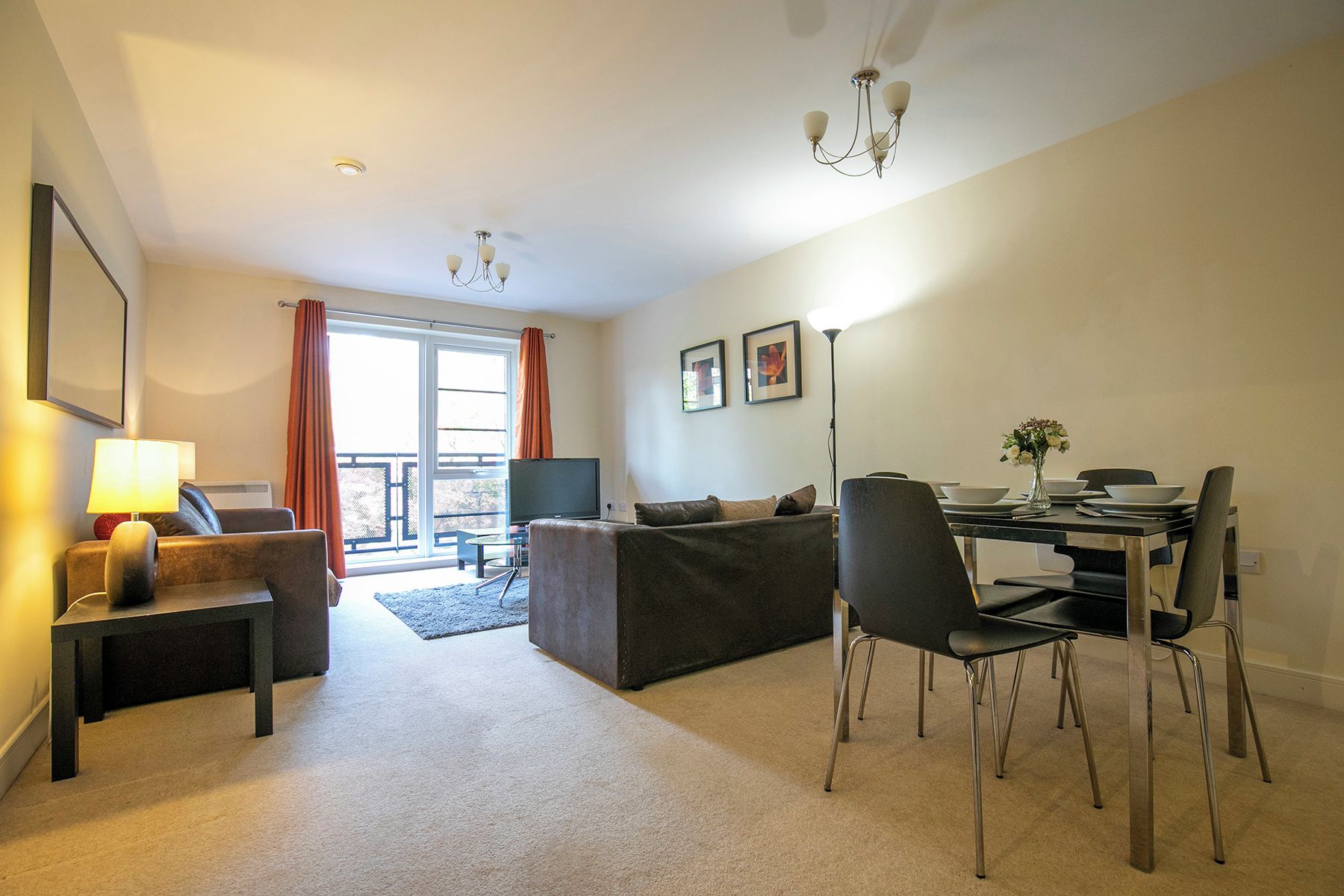 A living room with a sofa, a dining table set for two, and a TV.