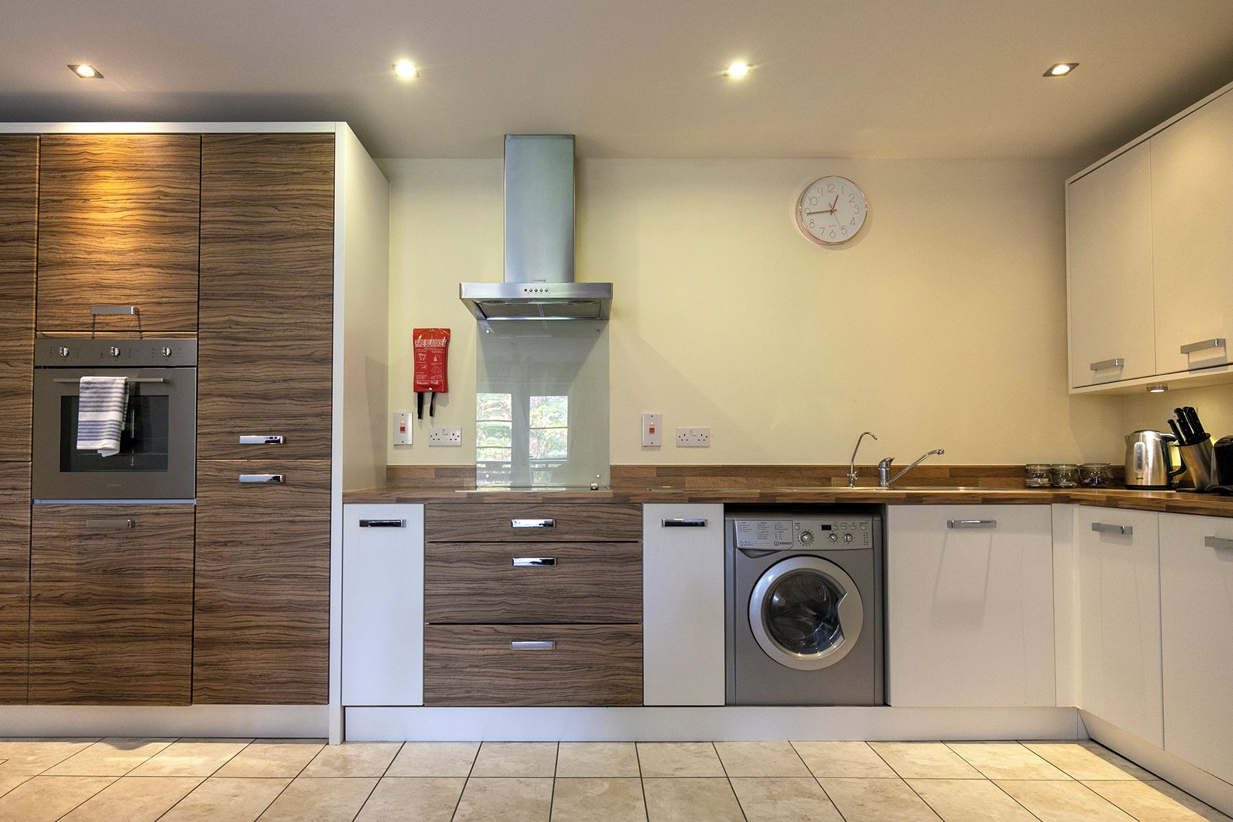 A modern kitchen with built-in appliances, a clock on the wall, and a window.