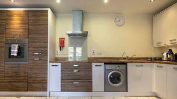 A modern kitchen with built-in appliances, a clock on the wall, and a window.