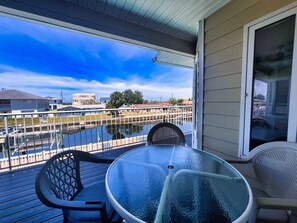 Ein Balkon mit Glastisch und Stühlen, der auf ein Gewässer und einen Yachthafen blickt.