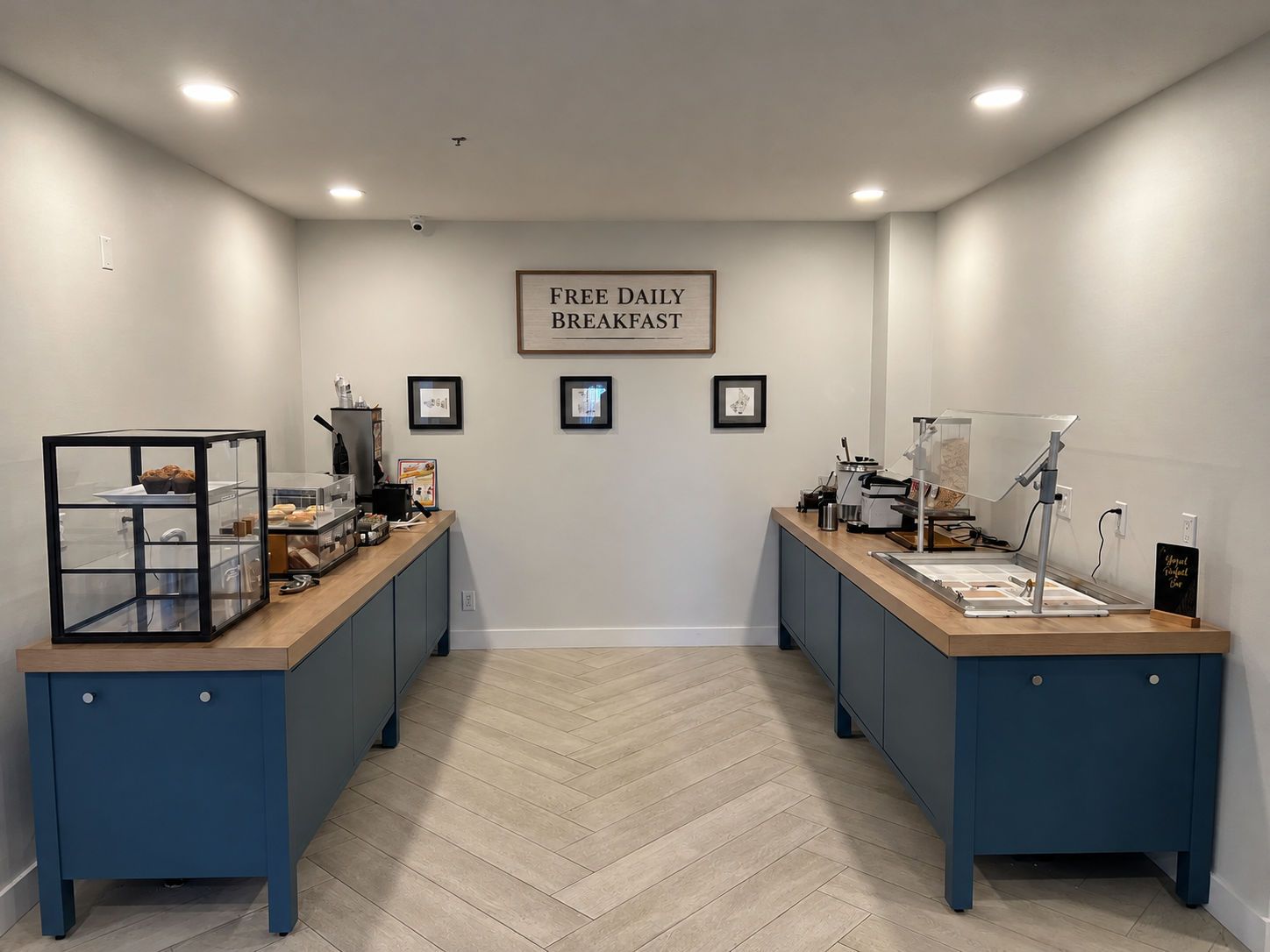 A breakfast area with two counters, a sign reading 'FREE DAILY BREAKFAST,' and framed pictures on the wall.