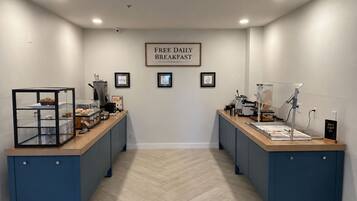 A breakfast area with two counters, a sign reading 'FREE DAILY BREAKFAST,' and framed pictures on the wall.