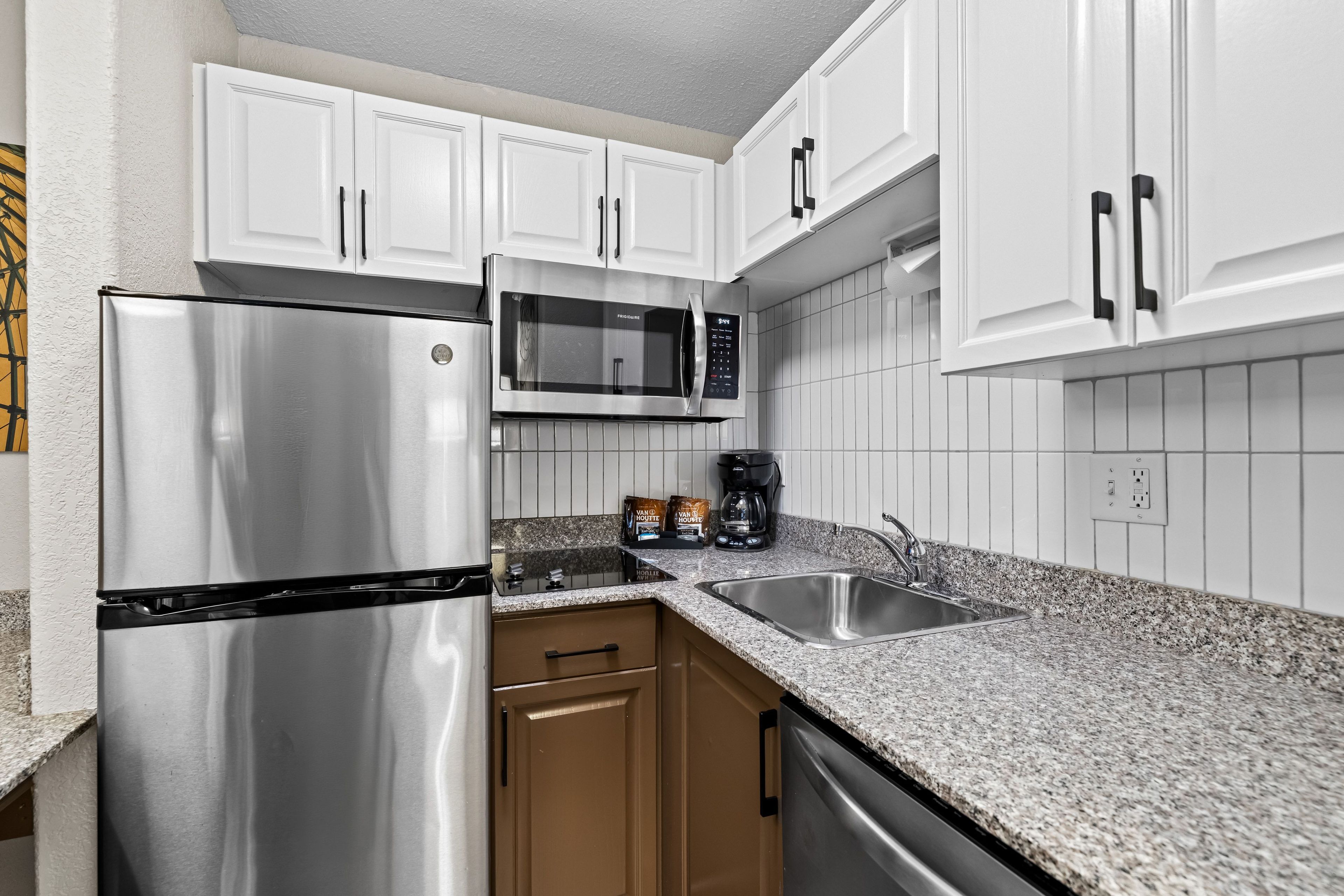A modern kitchen with stainless steel appliances, white cabinetry, and a granite countertop.