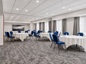 Un salón de conferencias con varias mesas y sillas, suelo alfombrado y un cuadro abstracto grande en la pared.