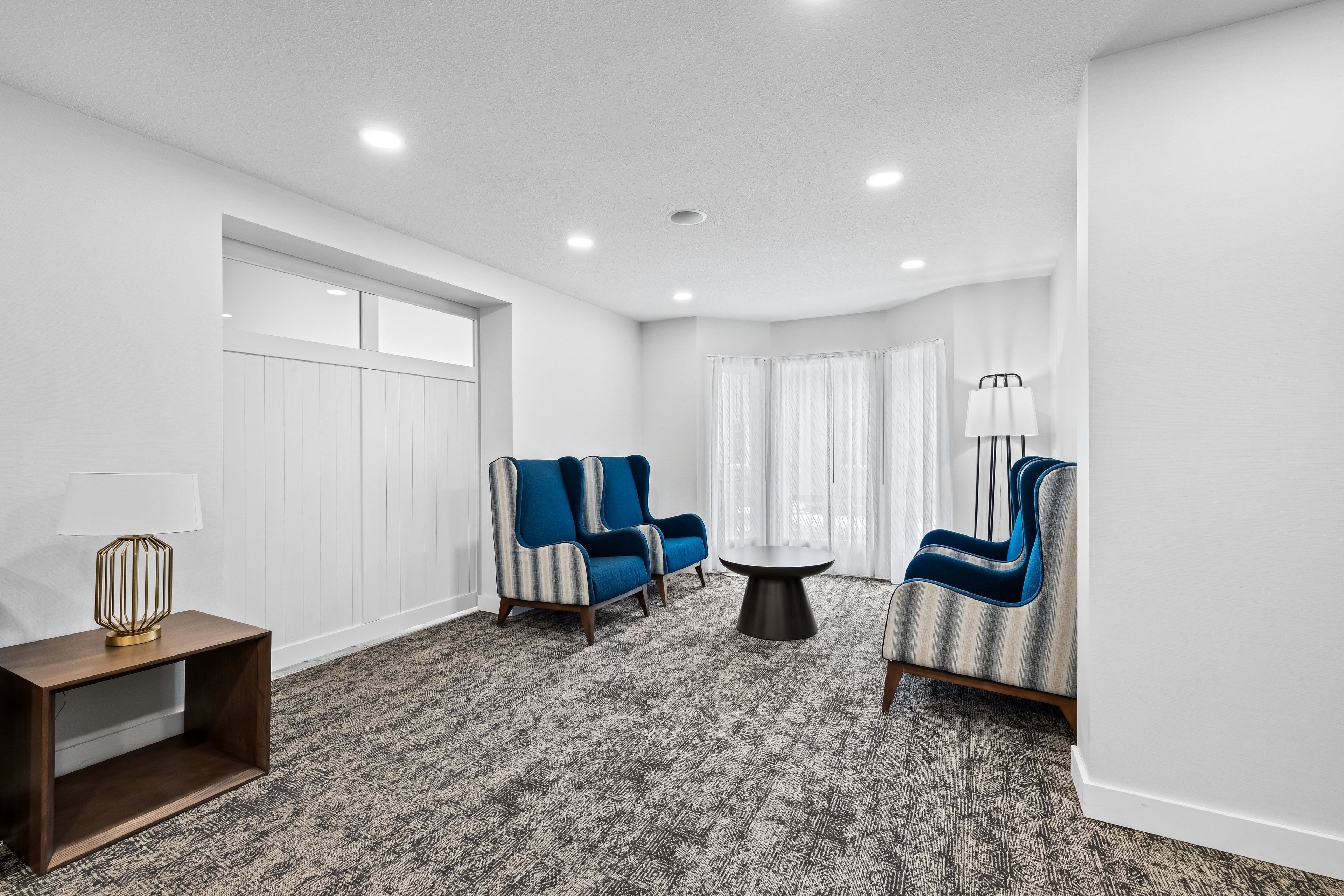 A modern living room with a patterned carpet, two armchairs, a small round table, and a lamp on a side table.