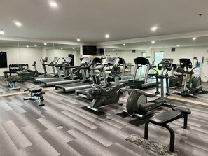 Un gimnasio bien iluminado con diversos equipos de ejercicio, incluyendo cintas de correr, elípticas y pesas libres.