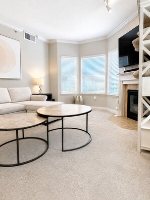 A living room with a sectional sofa, two round coffee tables, a fireplace, and a TV mounted on the wall. - Furnished Downtown SLC 2BR/2BA, 2 Garage Spaces, Desk, 30+ Nights (Salt Lake City)