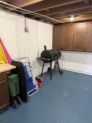 Un garage avec un barbecue, un chariot avec des sacs et une table en bois.