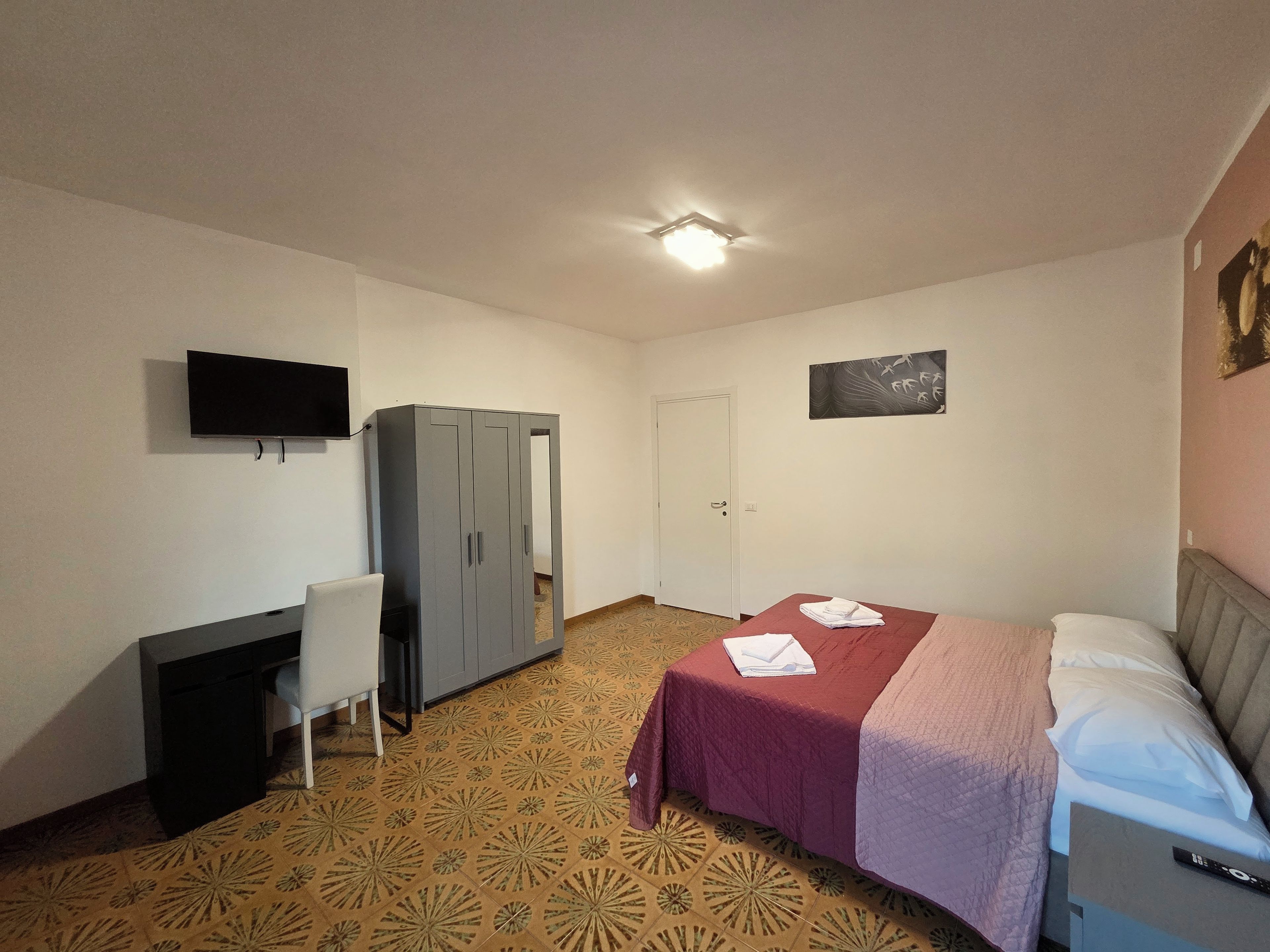 Ein Schlafzimmer mit Bett, Schreibtisch, Stuhl, Kleiderschrank, Fernseher und einer Tür.