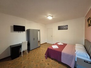 Une chambre à coucher comprenant un lit, un bureau, une chaise, une armoire, un téléviseur et une porte.