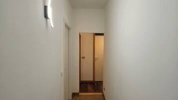 Un couloir étroit, avec un tapis à motifs, des murs blancs et une porte au fond.
