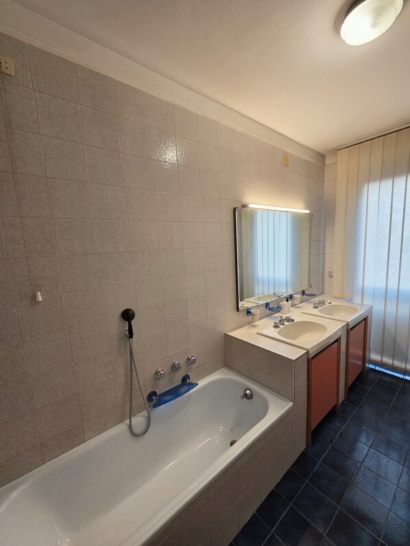 Ein Badezimmer mit einer Badewanne, zwei Waschbecken, einem Spiegel und einer Duschbrause.