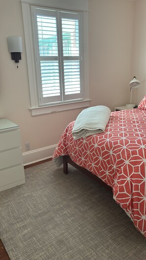 Un dormitorio con una cama, una mesita de noche, una lámpara, una ventana con persianas y un aplique de pared.