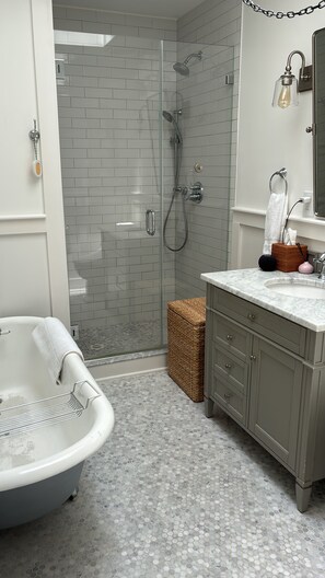 Un baño con ducha de vidrio, bañera independiente y tocador con encimera de mármol.